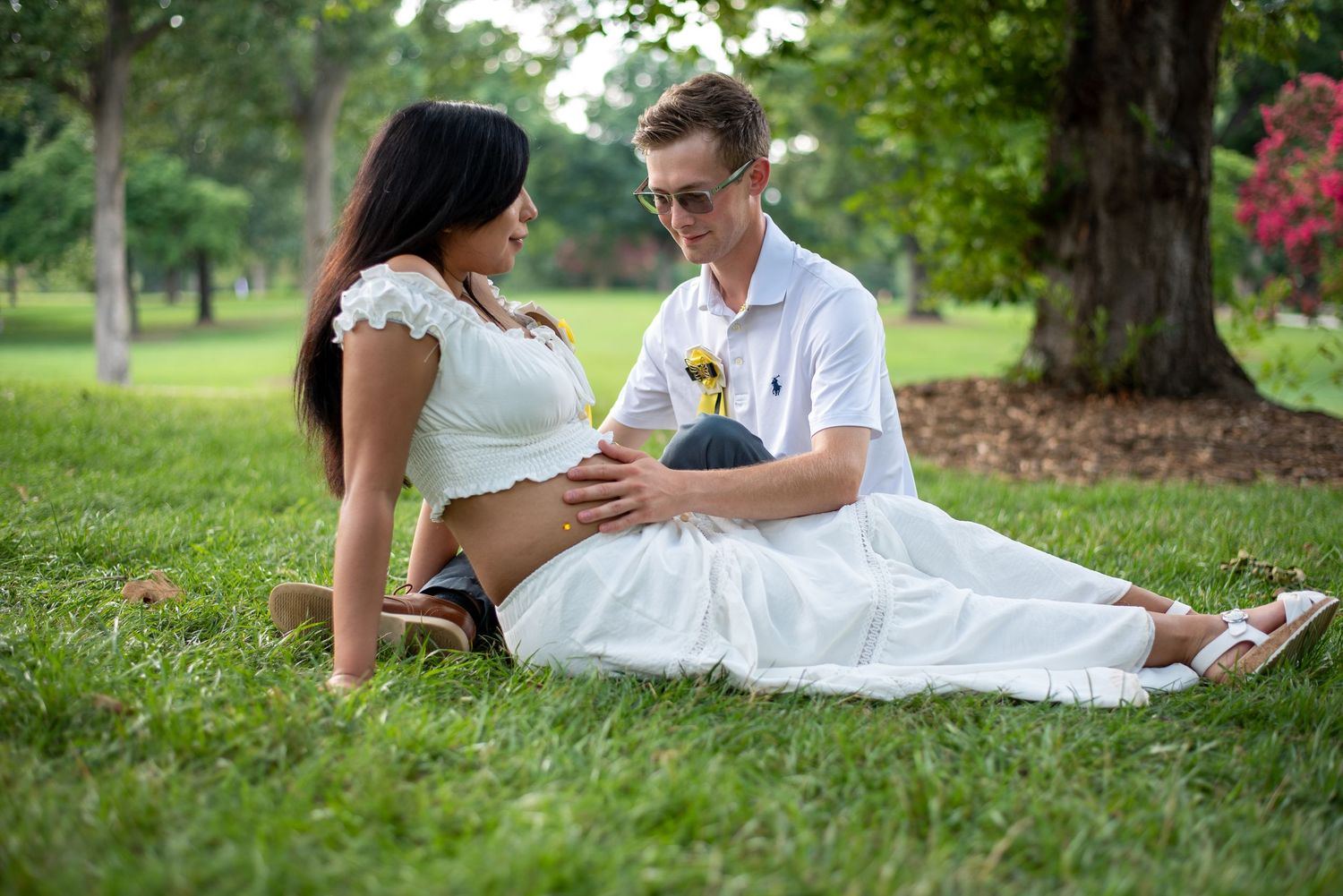 Pareja de novios sentada sobre el césped, riendo durante la sesión de fotos