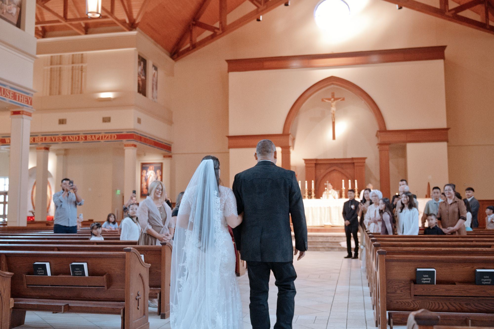 De espaldas, la novia avanza por el pasillo de la iglesia mientras la familia la mira desde las bancas